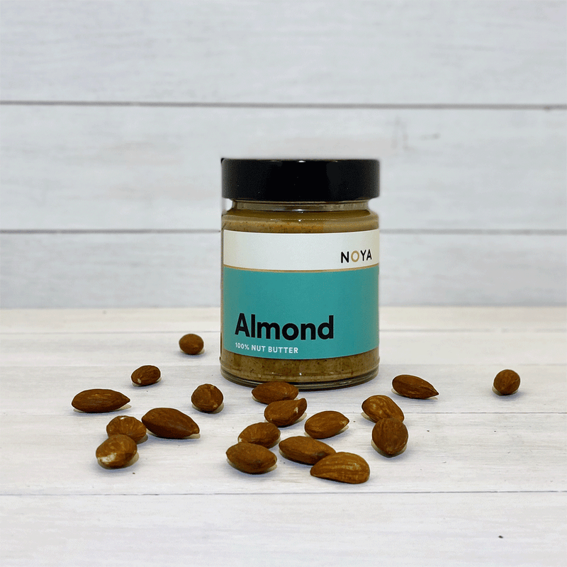 A glass jar of almond butter with almonds on a wooden table