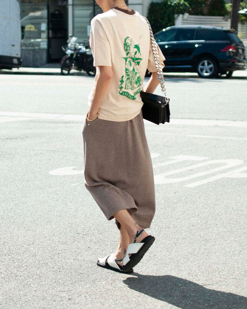 Back view of model in the street wearing brown knit pants, white sandals, and a beige ringer t-shirt.