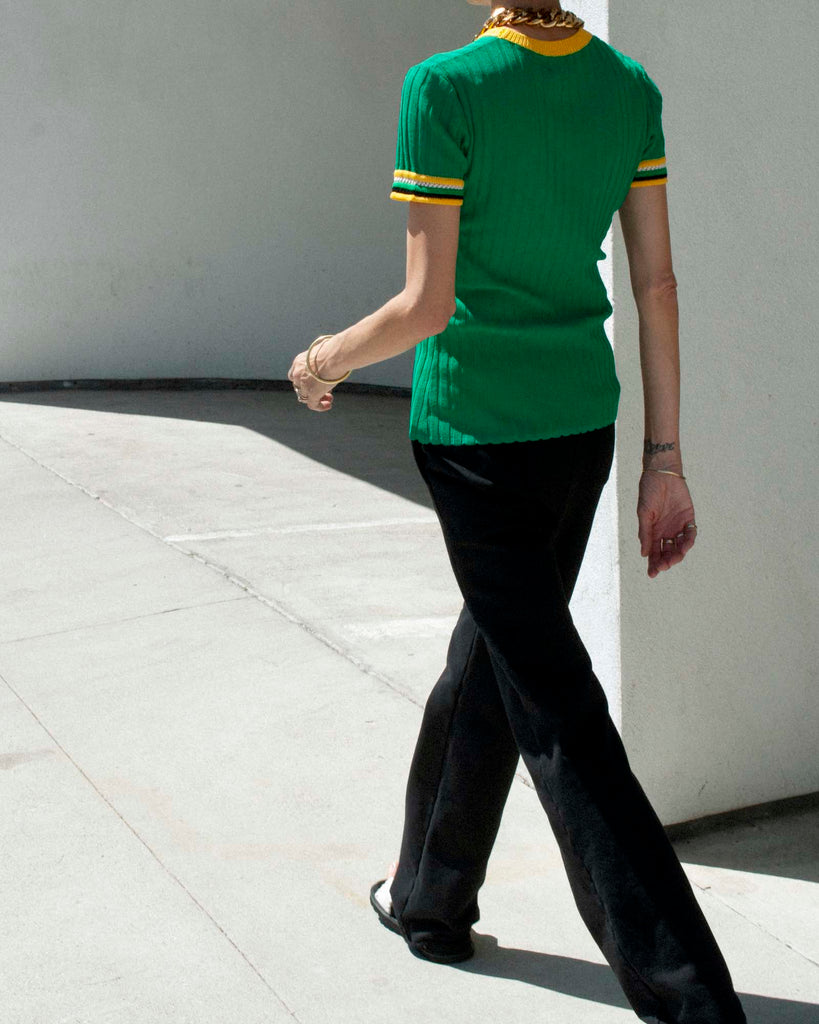 Back view of model walking wearing a green knitted t shirt and black tailored sweatpants.