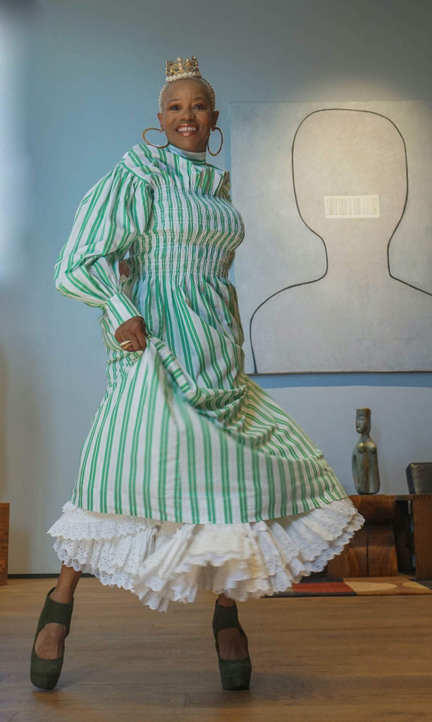 Starla stands indoors wearing a crown and green and white striped dress.