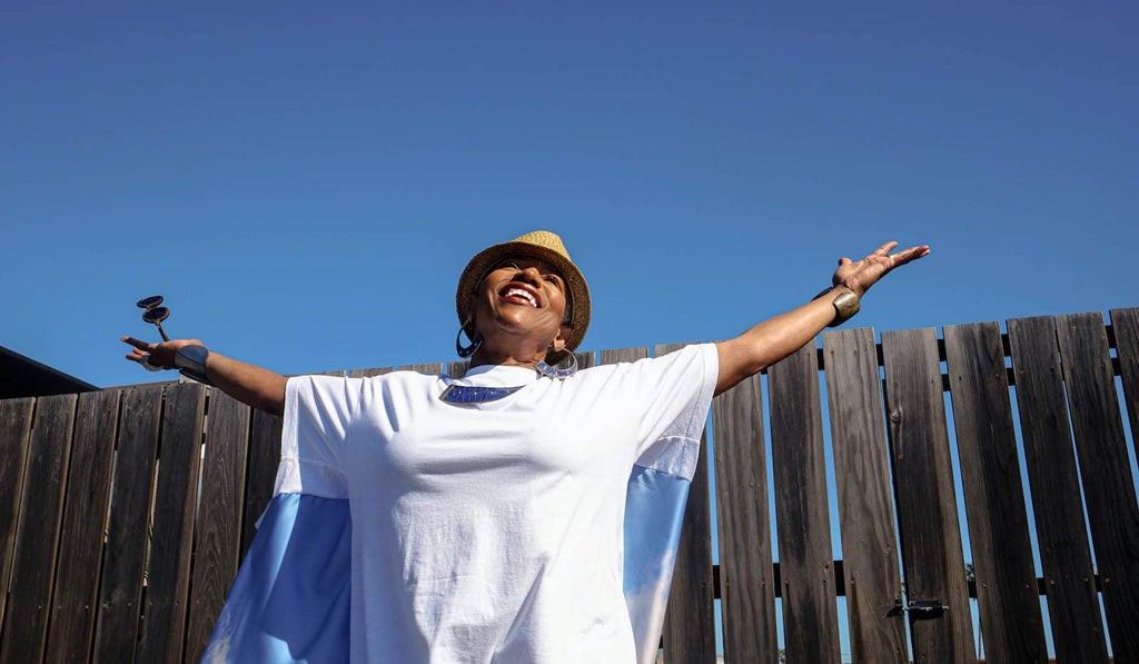 Starla stands outdoors with her arms wide, wearing a white t-shirt against the sky. 