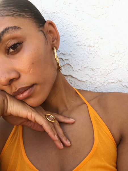 Close up of Courtney wearing an orange halter top and gold jewelry. 