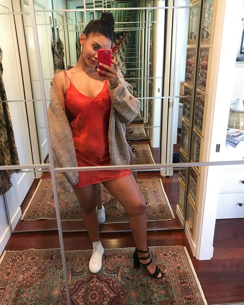 Courtney takes a mirror selfie wearing a red mini slip dress and beige cardigan.