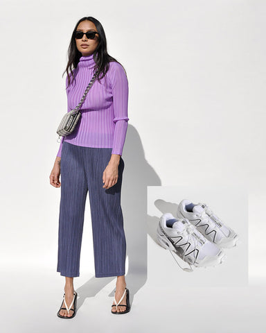 Photo of a model wearing a purple pleated mock neck long sleeve top and dark grey pleated pants.