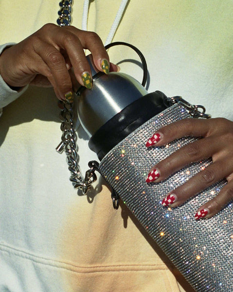 A detail photo of Evelynn's hands holding a rhinestone water bottle holder from Kara, and pulling a stainless steel bottle out.
