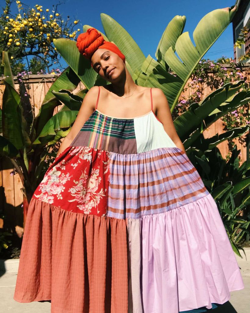 Courtney standing outdoors with greenery behind her, wearing a patchwork dress by La Réunion and holding the dress out to her sides. 