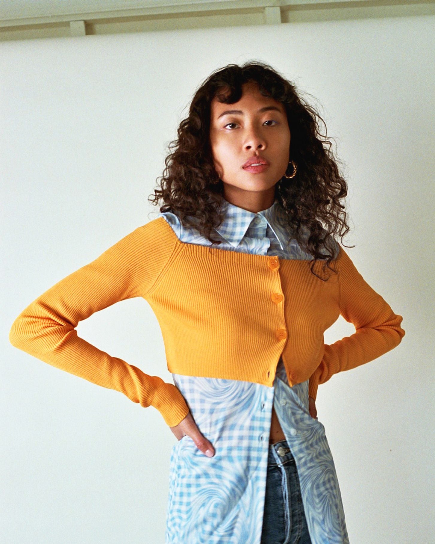 photo of model wearing a mesh checker blue button down worn under a bright orange cropped knit sweater