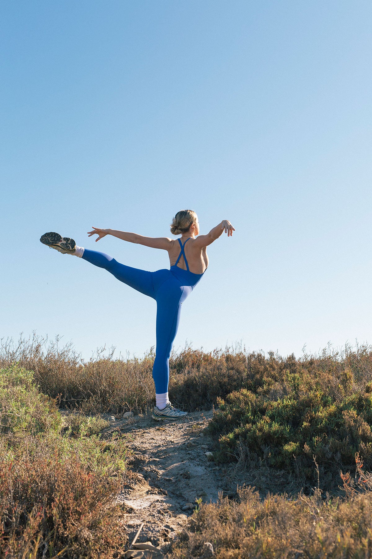 Wear One's At image of model extending leg on a hiking trail wearing a blue unitard