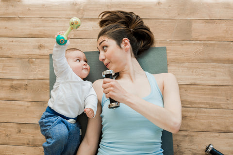 A woman lays on the floor while working out next to her child.