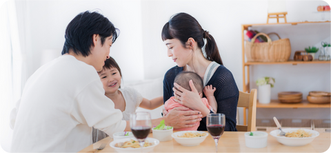 A mother, father, and their two small children sit at a dinner table having a meal.