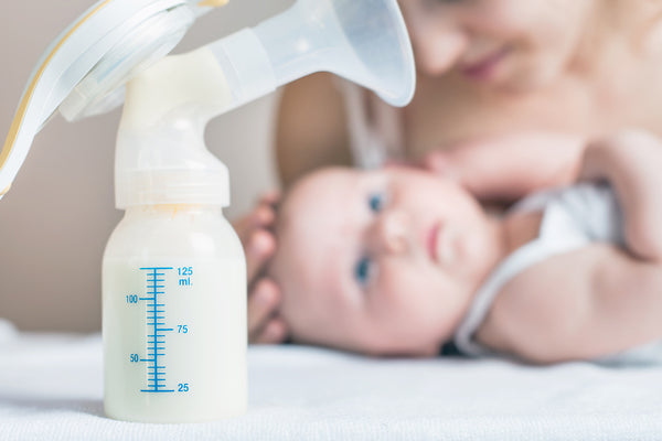baby on bed next to breast pump