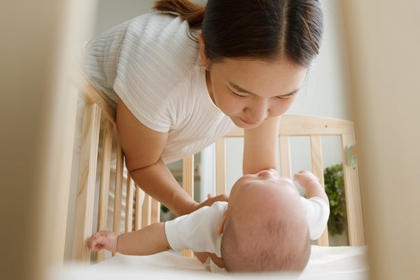 mother putting baby in crib