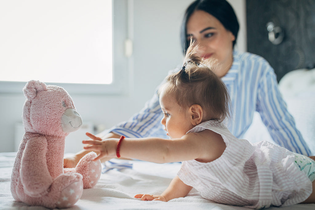 Mother and baby playing on the bed with a pink stuffed bear