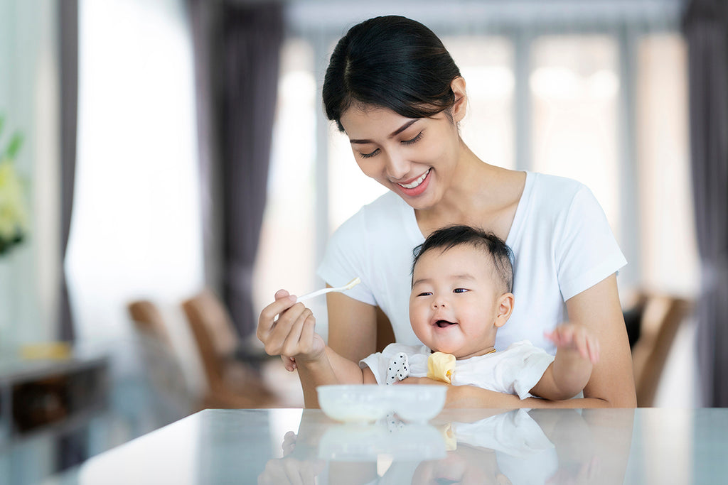 Mother sitting at dining table spoon-feeding her baby