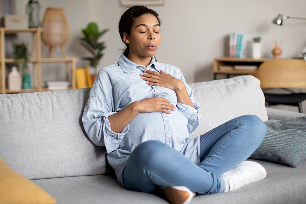 Pregnant woman sitting on couch holding her belly and taking a deep breath