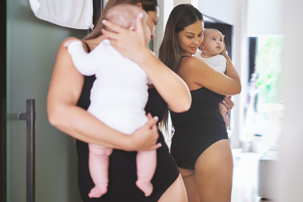 New mother holding child looking in the mirror at her postpartum underwear