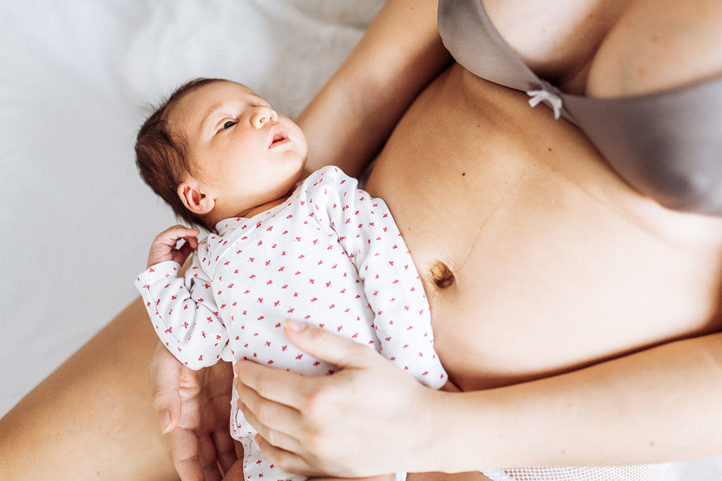 new mother in underwear holding newborn baby