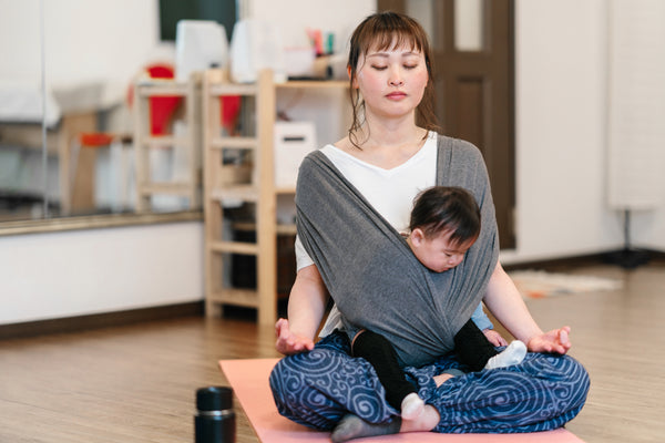 A woman meditates while holding her baby in a front sling wrap
