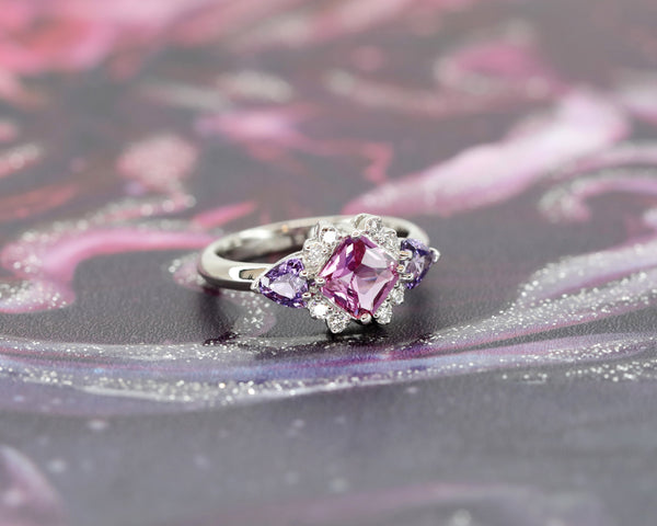 side view of platinum colored gemstone pink sapphire and side purple trillion shape gems and diamond ring custom made in montreal by bena jewelry on dark background