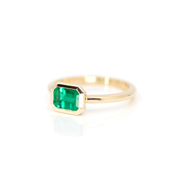 side view of emerald engagement ring custom made in montreal in yellow gold bezel setting by bena jewelry best canadian jewelry designer on white background