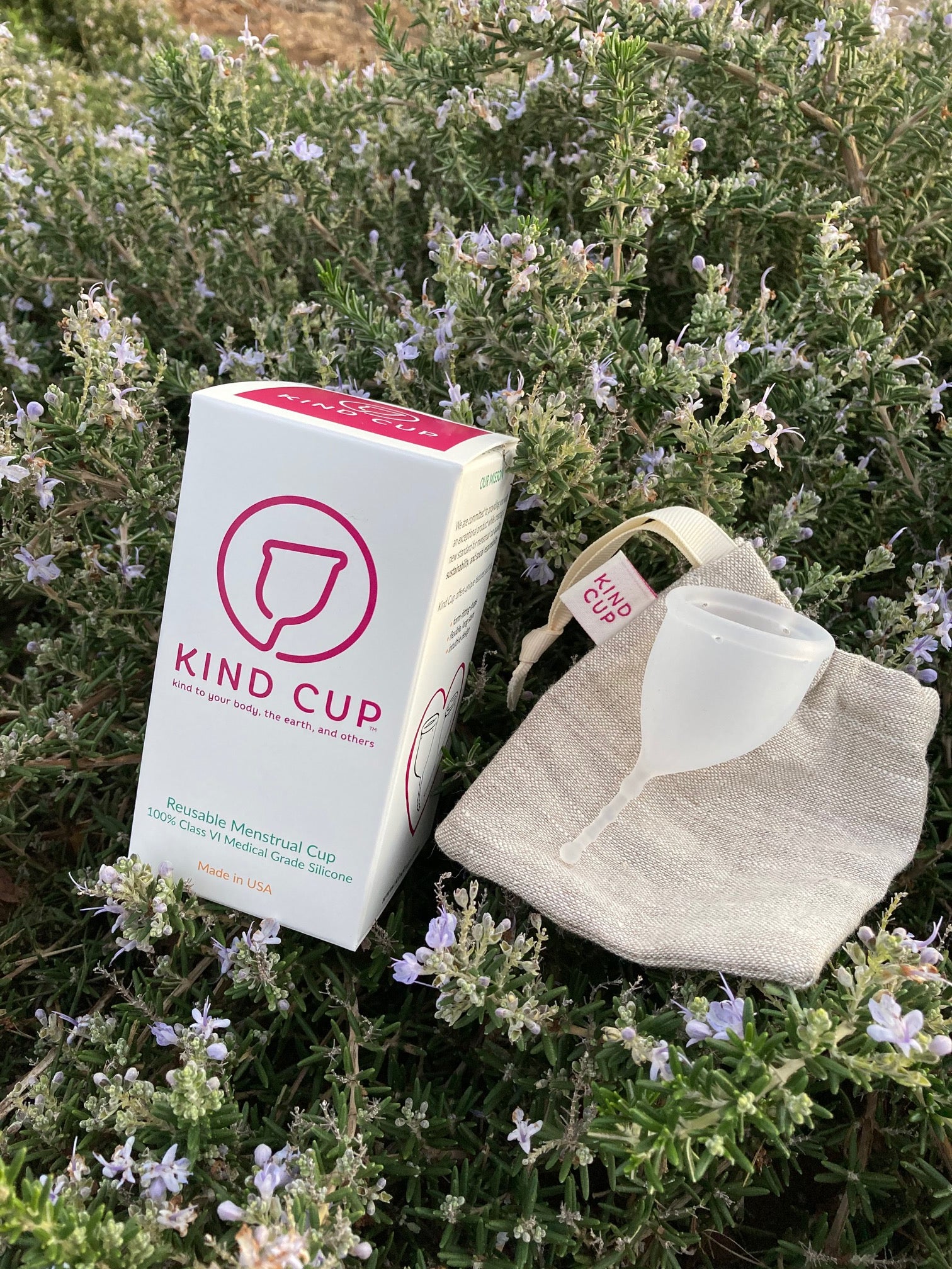 Kind Cup size small menstrual cup placed on earth-friendly linen bag and sustainable packaging all on a blooming rosemary bush