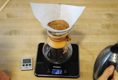 Wet coffee grinds in brewer siting on top of a scale, next to a timer