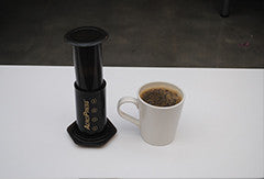 Aeropres plunger sitting next to coffee mug
