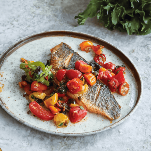 Grilled fish with colorful cherry tomatoes and herbs on a ceramic plate.