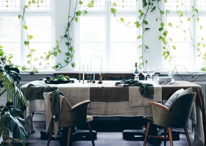 large dining table with layers of linen tablecloths and hanging green ivy decor