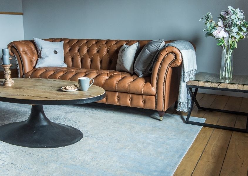 brown leather chesterfield sofa with rustic coffee table and blue rug