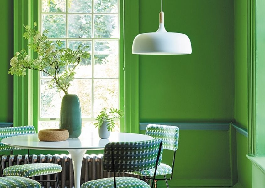 Dining room with bright green walls, large window, white round dining table and white hanging pendant light