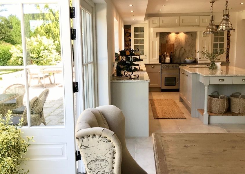 View of grey wooden kitchen with white french doors open to garden