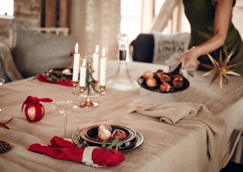 Woman laying Christmas dining table with beige table cloth, red linen napkins and gold star