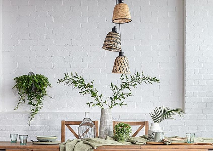 Three hanging bamboo pendant lights over dining table with green leaves in tall vase