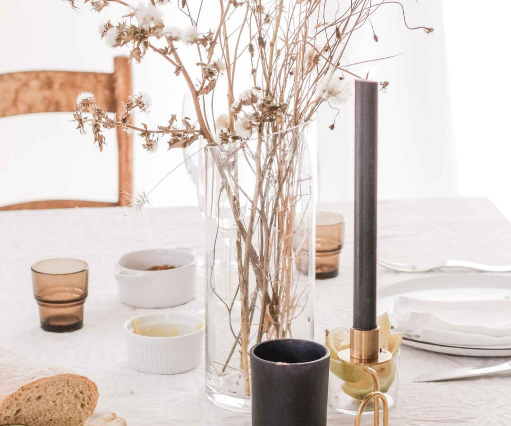 Large glass vase with dried flowers on dining table with white table cloth