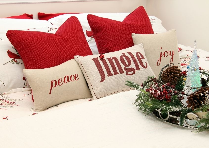 Christmas cushions on a white bed with pine cone Christmas display