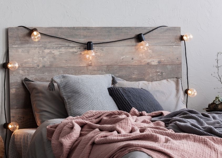 Wooden bed with fairy lights on headboard and scattered cushions