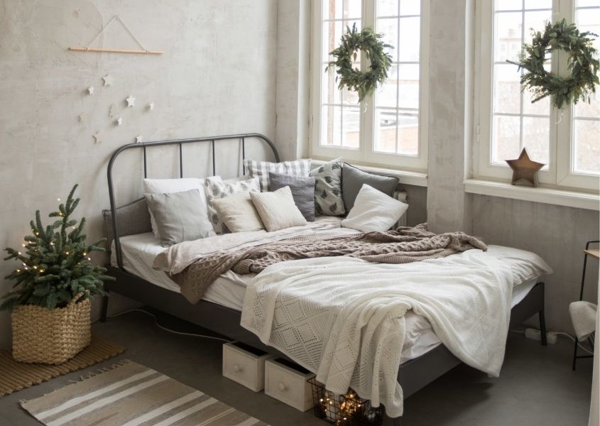 Metal double bed frame in bedroom decorated with hanging christmas wreaths on window and small Christmas tree