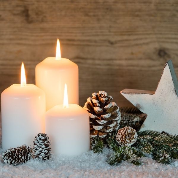 White lit Christmas candles with frosted pine cone against wood wall