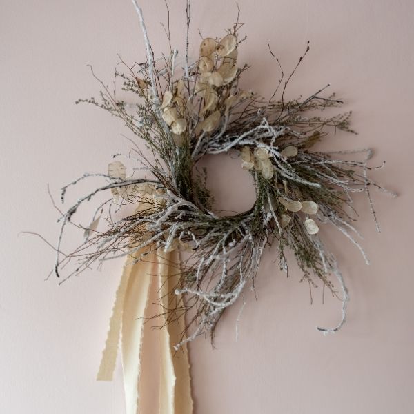 Modern wreath of long twigs and dried flowers with cream ribbon on neutral coloured wall
