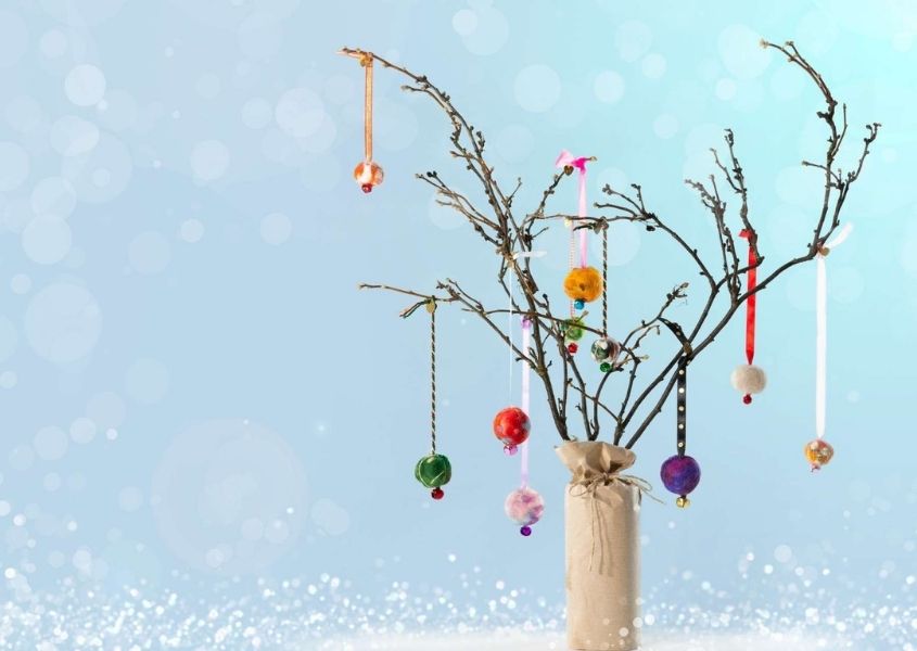 Twigs in a vase with hanging Christmas decorations on a blue background