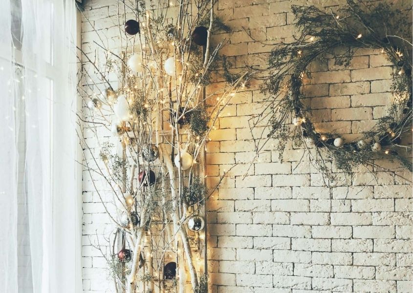 Rustic and natural Christmas decorations with wreath and homemade tree made from twigs and leaves against brick wall