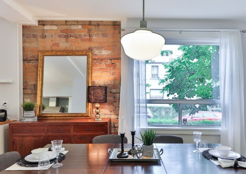Dining room with exposed brick wall with large mirror and glass pendant ceiling light