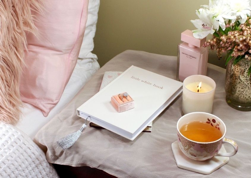 bedside table with book, cup of tea, candle and flowers