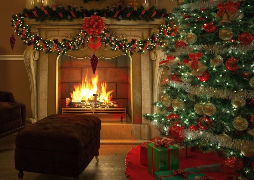 Traditional decorated Christmas tree next to large stone fireplace with open fire