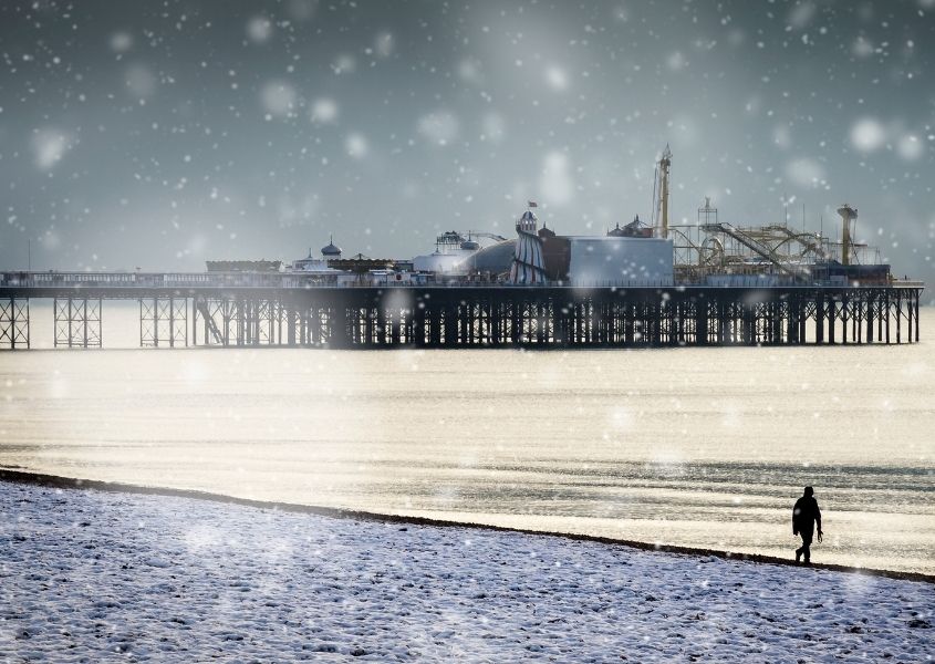 Brighton Pier and beach in the snow with person walking on the pebbles
