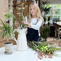 woman arranging flowers in a jug on a reclaimed wood dining table