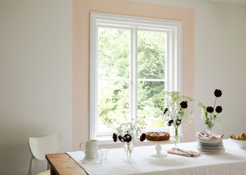 White sash window with light pink border painted around it and neutral coloured wall with white dining table