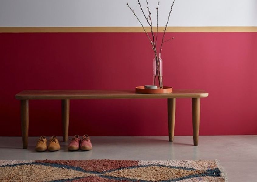 Wall painted in deep red shade and white with wooden bench and boots