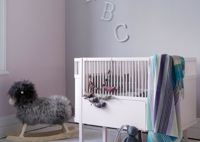 Nursery with white painted cot and pastel coloured walls with chair and grey faux fur throw